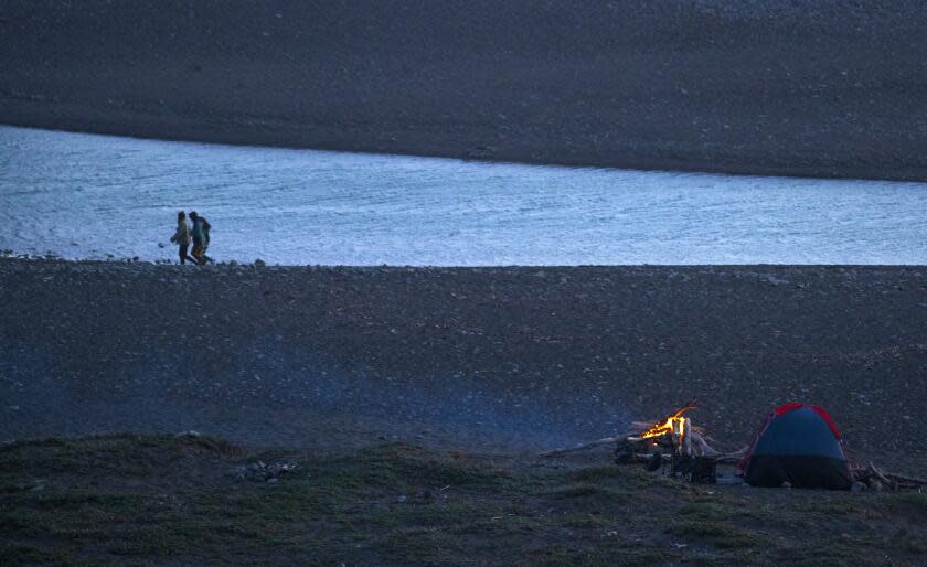 BIG SUR, CA - MAY 01: Beachgoers walk along the shore as a campfire glows on the beach at San Carpoforo Creek on California Highway 1 near Ragged Point on Saturday, May 1, 2021 in Big Sur, CA. (Brian van der Brug / Los Angeles Times)