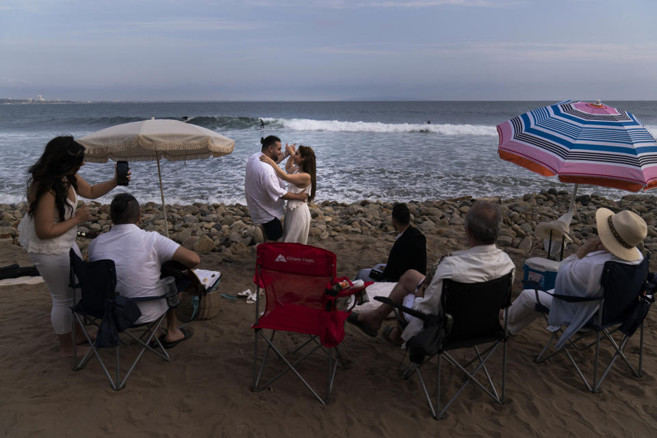 Pejiman Sabet and his wife, Gili, dance in front of their family members on Topanga Beach in Malibu, Calif., Tuesday, Sept. 28, 2021, as a surfer rides a wave in the distance. The couple, who were fully vaccinated, said the gathering was just to appreciate life. "Love is everything right now," said the wife. (AP Photo/Jae C. Hong)