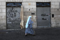 FILE - In this March 15, 2021, file photo, a nun wearing a face mask to curb the spread of COVID-19, walks past a closed shop in downtown Rome. Lofty hopes that the crisis would encourage a new and tighter bloc to face a common challenge have given way to the reality of division: The pandemic has set member nation against member nation, and many capitals against the EU itself, as symbolized by the disjointed, virtual meetings leaders now hold. In Italy, Premier Giuseppe Conte was forced to resign over his handling of the economic fallout of the pandemic. (AP Photo/Alessandra Tarantino, File)