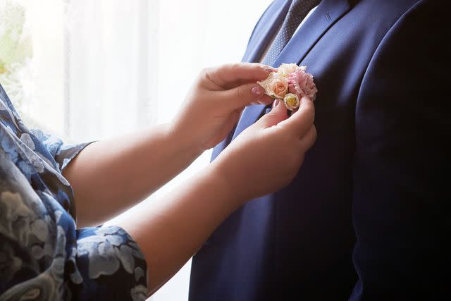 <p>Getty</p> groom's mother adjusts the boutonniere on his suit