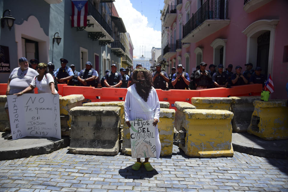 A demonstrator dressed as Jesus holds a Spanish message: "Children of the cane field fight for Puerto Rico," in front of a police perimeter around the La Fortaleza residence of Gov. Ricardo Rosselló in San Juan, Puerto Rico, Wednesday, July 17, 2019. Protesters are demanding Rosselló step down for his involvement in a private chat in which he used profanities to describe an ex-New York City councilwoman and a federal control board overseeing the island's finance. (AP Photo/Carlos Giusti)