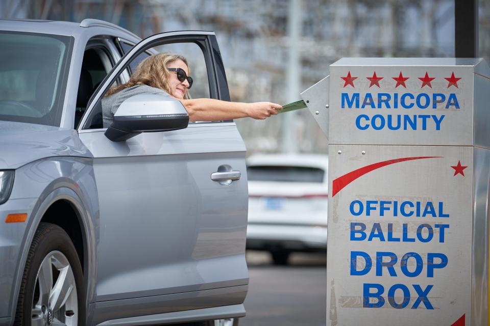 Shana Hofberger leans out of her car door to place her ballot in the ballot drop box outside the Maricopa County Tabulation and Elections Center in Phoenix for Arizona’s Aug. 2, 2022, primary election.