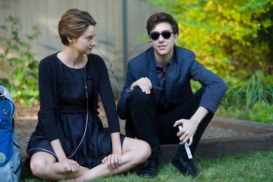 teens sitting on the grass sharing earphones to listen to music