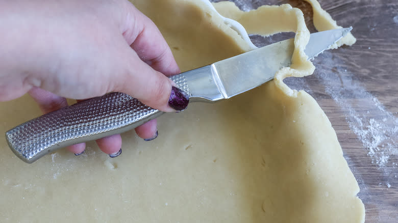 a knife cutting the edges off of quiche dough
