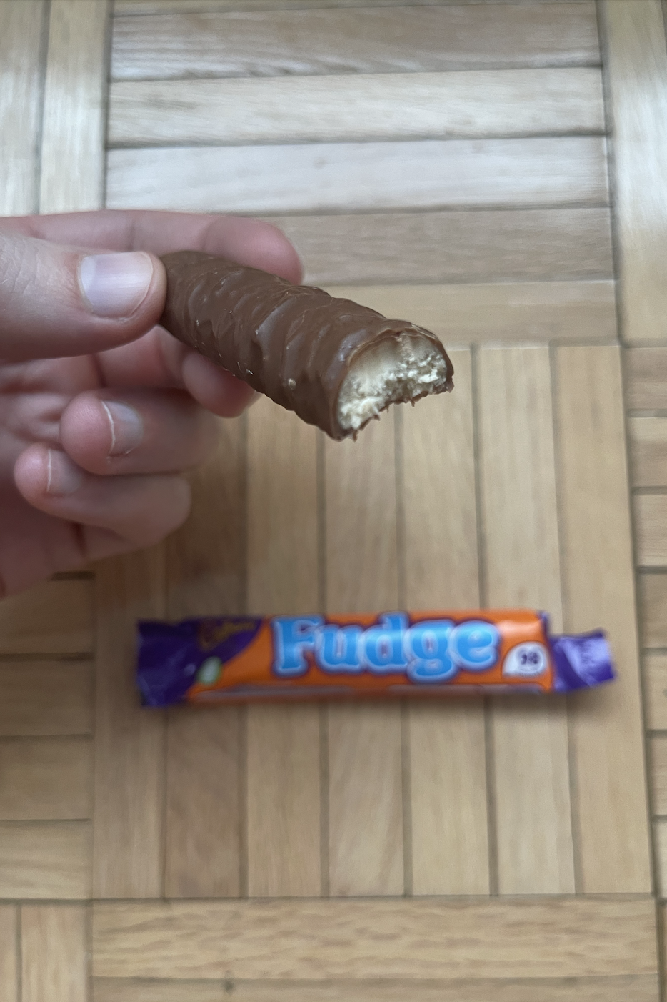 Person holding a half-eaten Fudge chocolate bar with an unopened one below