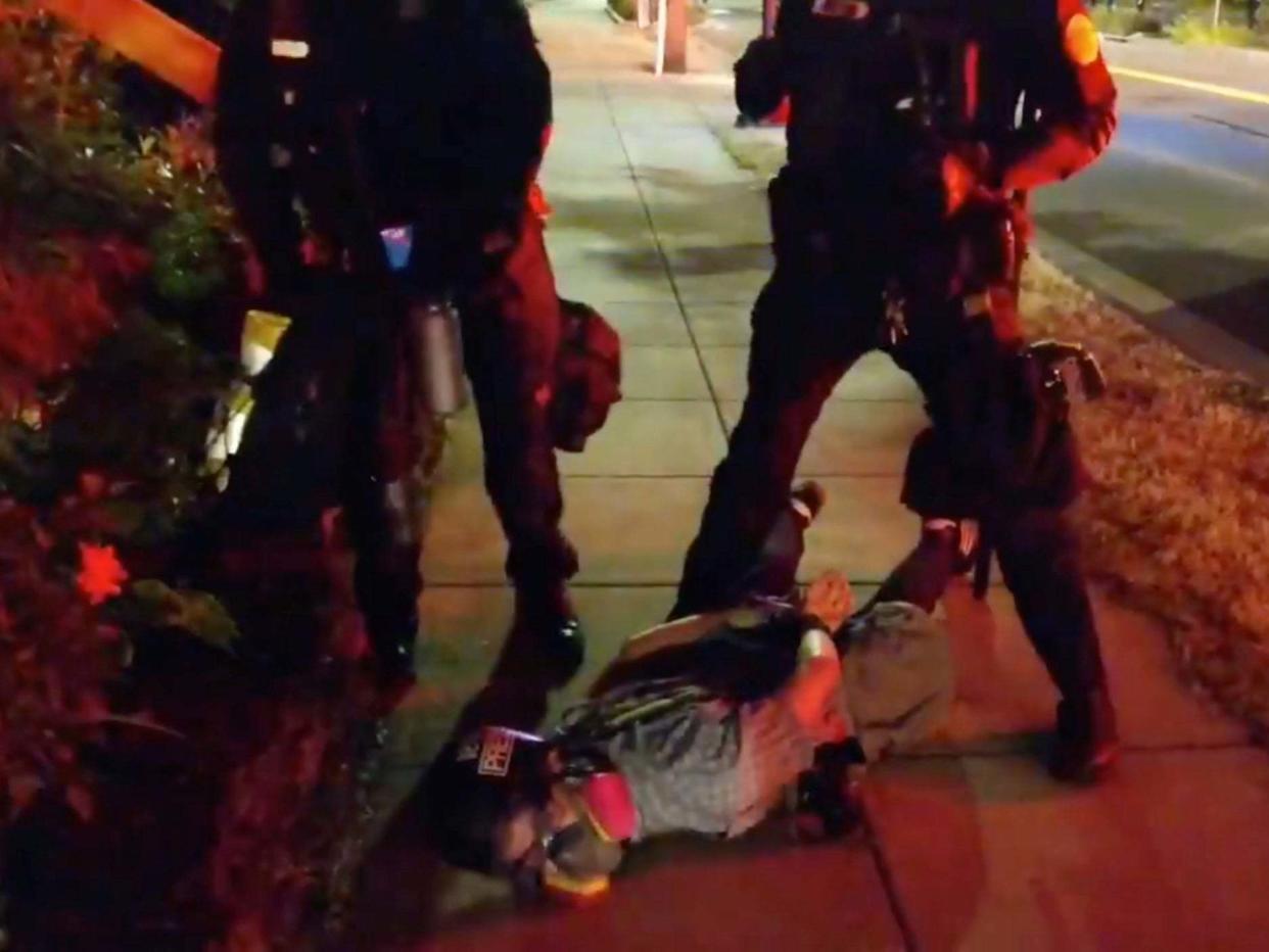 Journalist Justin Yau lies handcuffed on the ground with police officers standing over him at a demonstration in Portland, Oregon: ALEX MILAN TRACY via REUTERS
