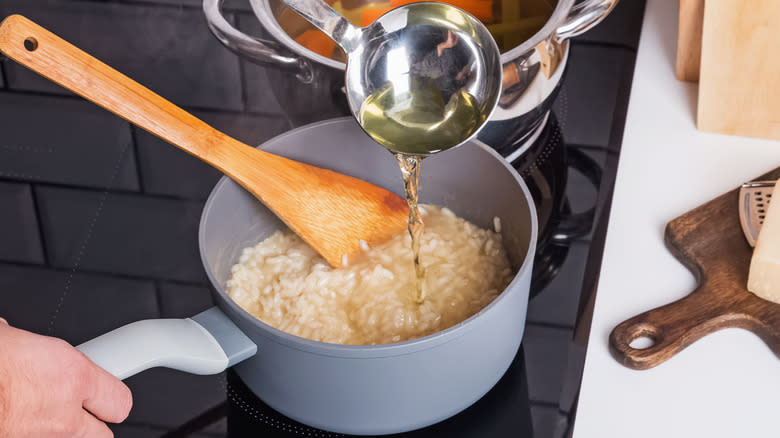 Pouring broth from ladle into rice on stove top