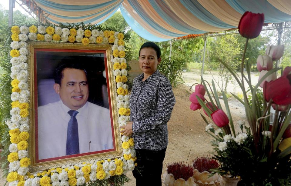 In this Nov. 20, 2016 photo, Kem Thavy stands by a portrait of her brother Kem Ley at his grave in Ang Takok, Cambodia. Kem Ley, a poor rice farmer's son turned champion of Cambodia's have-nots, was sipping his usual iced latte in the same chair he had occupied most mornings for years when a former solider he may never have met walked into the Caltex gas station cafe. Armed with a semi-automatic Glock pistol, the assassin fired into his chest and head, execution-style. Then he walked casually away from the scene. (AP Photo/Denis Gray)