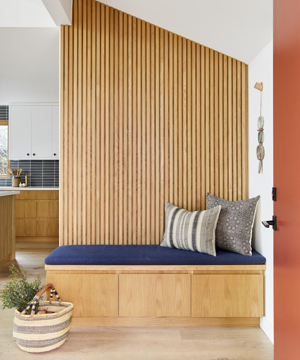 Modern entryway bench ideas with a white oak storage bench with drawers, blue upholstered seat cushions, and white oak slatted panel on wall behind