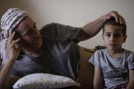Ali Kinno comforts his son Ahmad at a temporary apartment in the coastal town of Jiyeh, south of Beirut, Lebanon, Tuesday, Sept. 15, 2020. The Kinno family from Syria's Aleppo region was devastated in the wake of the Aug. 4 explosion at the Beirut port -- Hoda, 11, suffered a broken neck and other injuries and her sister Sedra, 15, died in the explosion. (AP Photo/Hassan Ammar)