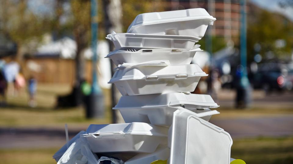 White styrofoam used food containers stacked in trash can in park.