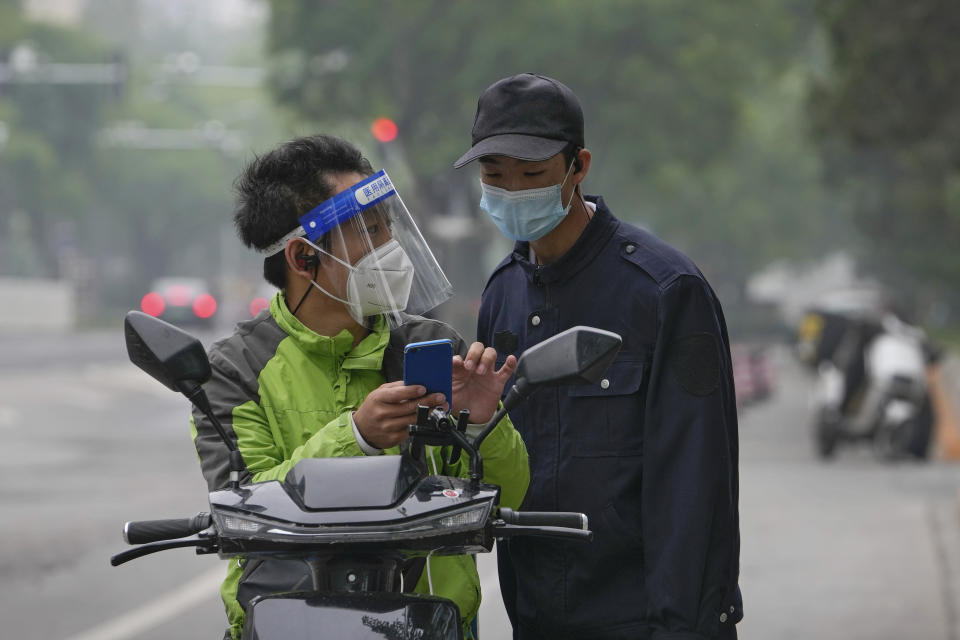 A delivery worker wearing a face shield and a mask asks for a direction from a security guard near a shuttered mall in the central business district on Tuesday, May 10, 2022, in Beijing. Beijing, the capital, began another round of three days of mass testing for millions of its residents Tuesday in a bid to prevent an outbreak from growing to Shanghai proportions. (AP Photo/Andy Wong)