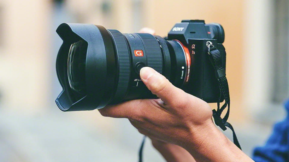Photographer's hands holding Sony FE 12-24mm f/2.8 G Master mounted to Sony A7 camera