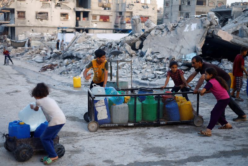 FILE PHOTO: A Palestinian man and children push a cart with water containers, amid the ongoing conflict between Israel and Hamas, in southern Gaza City, in the Gaza Strip