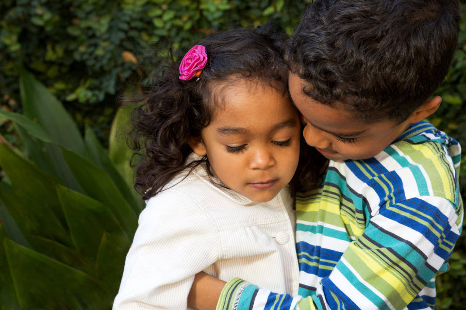 Young boy hugging his sister, both with calm expressions in a natural setting