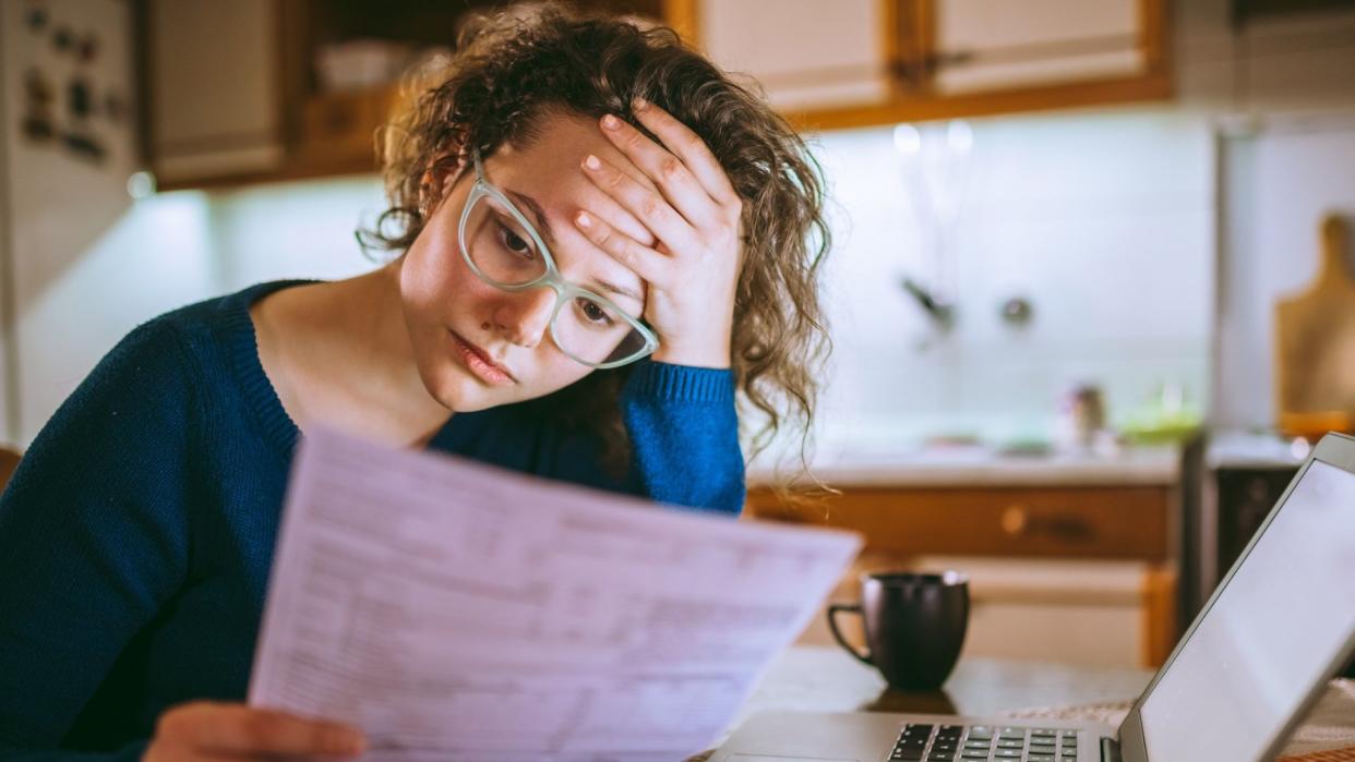 Young brunette curly female reading her bill papers, looking stressed.