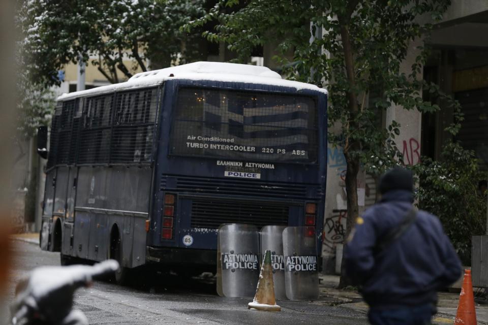 A policeman walks outside the Pan-Hellenic Socialist Movement (PASOK) offices after a gunman opened fire at the bus, left, in Athens, on Tuesday, Jan. 10, 2017. Authorities say a police officer has been wounded after shots were fired outside the offices of the political party in an area of Athens where anarchist groups frequently clash with police and attack symbols of authority. (AP Photo/Thanassis Stavrakis)