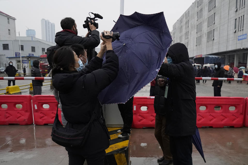 A plainclothes security person uses his umbrella to block journalists from filming after the World Health Organization team arrive at the Baishazhou wholesale market on the third day of field visit in Wuhan in central China's Hubei province on Sunday, Jan. 31, 2021. (AP Photo/Ng Han Guan)