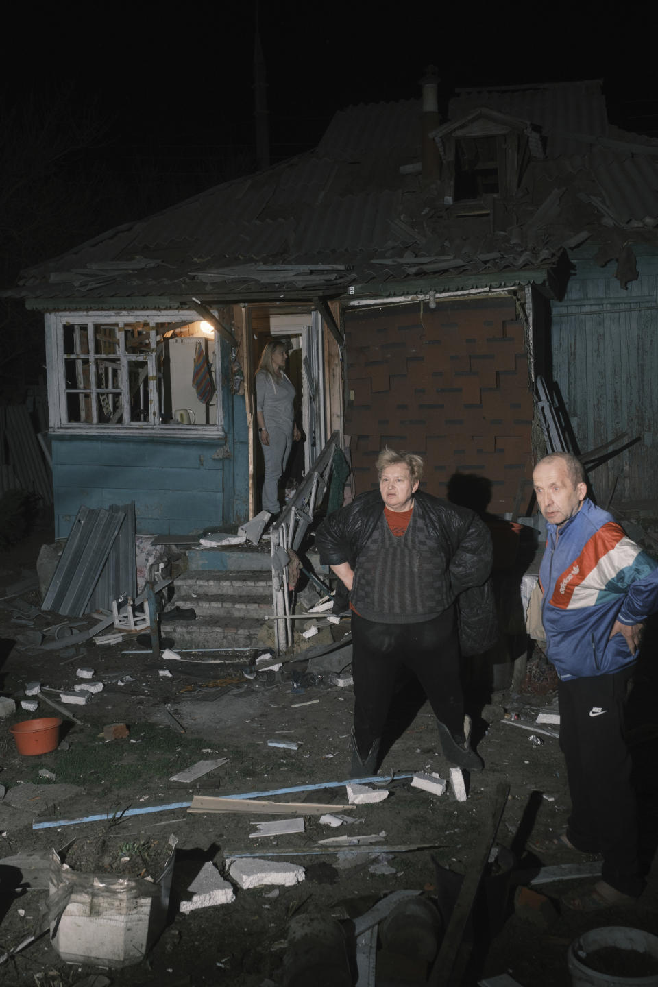 Family looks on their house which was damaged after a Russian drone strike on residential neighborhood in Kharkiv, Ukraine, on Thursday, April 4, 2024. (AP Photo/George Ivanchenko)