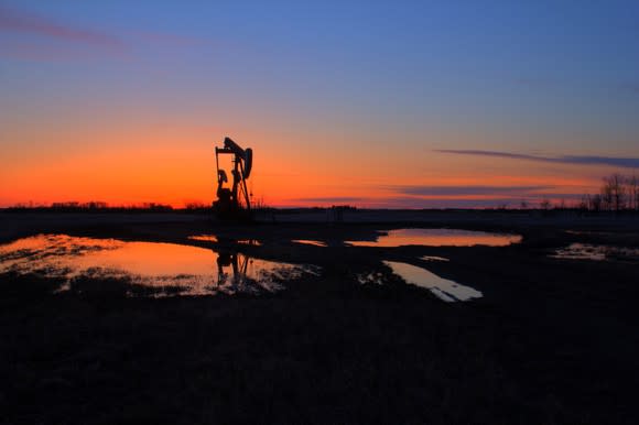 Pump jack backlit by the setting sun after the rain.