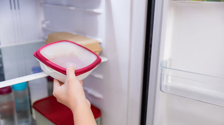 hand putting tupperware in the fridge