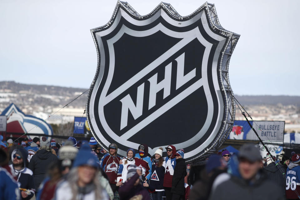 FILE - In this Feb. 15, 2020, file photo, fans pose below the NHL league logo at a display outside Falcon Stadium before an NHL Stadium Series outdoor hockey game between the Los Angeles Kings and Colorado Avalanche, at Air Force Academy, Colo. The NHL announced Friday, Dec. 17, 2021, that it was postponing all games for the Colorado Avalanche and Florida Panthers through at least next weekend amid worsening COVID-19 test results across the league. (AP Photo/David Zalubowski, File)