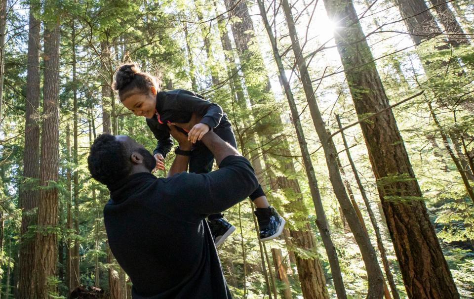 A man lifts up his daughter and they share a tender moment in a sunlit forest park - Getty
