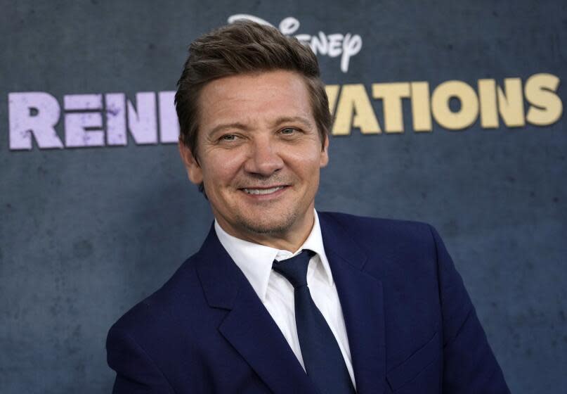 Jeremy Renner in a blue suit and tie smiling and looking to the side