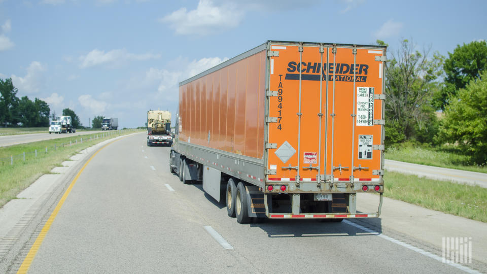 An orange Schneider trailer being pulled on a highway