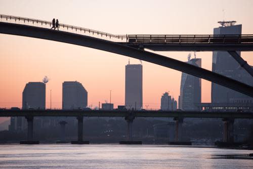 People walk on a bridge over the Han river before the city skyline in Seoul early on January 16, 2017. / AFP PHOTO / Ed JONESED JONES/AFP/Getty Images