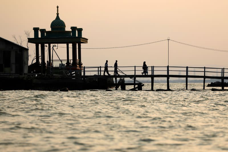 Muslims walk on a bridge at Bedono, a village affected by rising sea level and land subsidence in Demak regency near Semarang