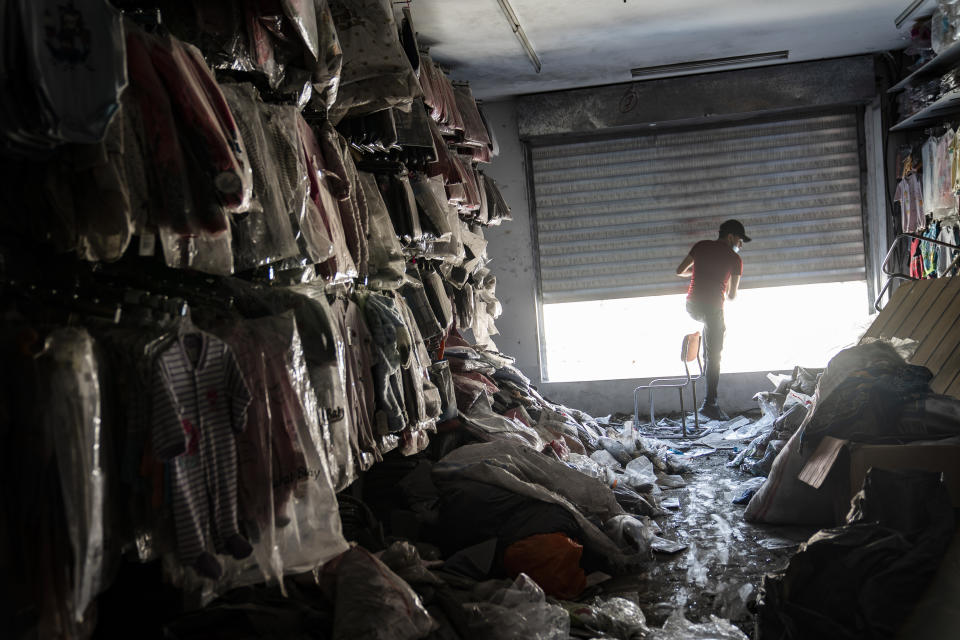 Ali el-Bably, 24, a small business employee, opens the second floor windows as he works to clean concrete dust and debris from a shop after an air-strike destroyed a neighboring building prior to a cease-fire that halted a 11-day war between Gaza's Hamas rulers and Israel, Tuesday, May 25, 2021, in Gaza City, the Gaza Strip. (AP Photo/John Minchillo)