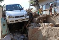 Residents remove debris from their home, around a crushed car, one day after a landslide hit a residential area in Hiroshima, western Japan, on August 21, 2014