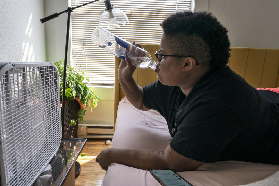 FILE - Katherine Morgan drinks water in front of a box fan while trying to stay cool in her downtown apartment without air conditioning on Thursday, Aug. 12, 2021, in Portland, Ore. People have headed to cooling centers as the Pacific Northwest began sweltering under another major, multi-day heat wave. (AP Photo/Nathan Howard, File)