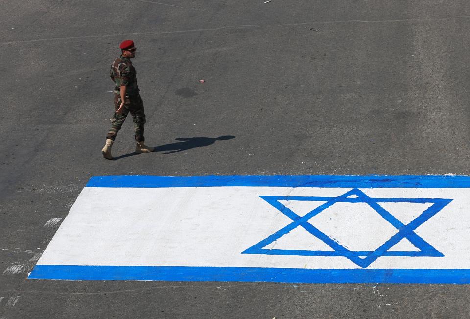 A fighter with Iraqi Popular Mobilization Forces walks past a representation of an Israeli flag during "al-Quds" Day, Arabic for Jerusalem, in Baghdad, Iraq, Friday, May 31, 2019. Jerusalem Day began after the 1979 Islamic Revolution in Iran when the Ayatollah Khomeini declared the last Friday of the Muslim holy month of Ramadan a day to demonstrate the importance of Jerusalem to Muslims. (AP Photo/Khalid Mohammed)