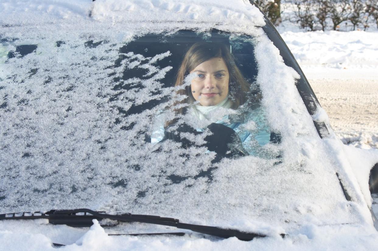 A woman in her car with snow covering her windshield