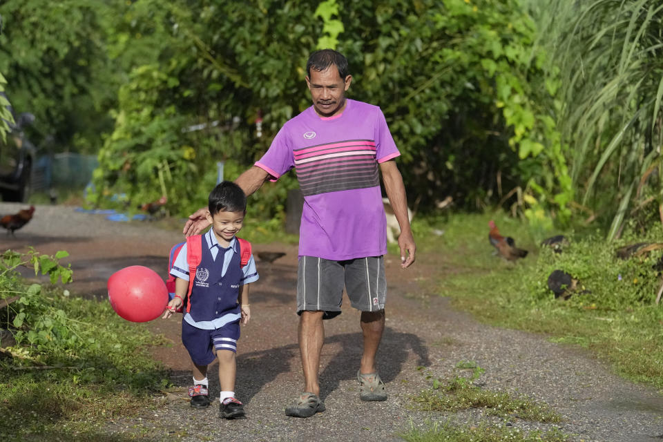 Tawee Lasopha and his grandson Thanathorn Sopha, son of his daughter Maliwan Lasopha who was killed in a knife and gun attack at The Young Children's Development Center, walk to catch a school bus in the rural town of Uthai Sawan, in Nong Bua Lamphu province, northeastern Thailand, Thursday, Oct. 5, 2023. On Friday, Oct. 6, Tawee marks the first anniversary of the death of his daughter Maliwan Lasopha. (AP Photo/Sakchai Lalit)