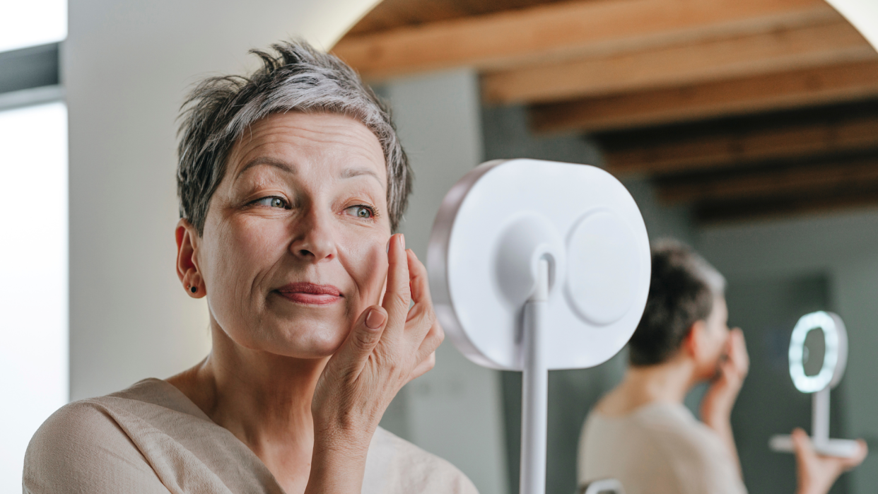 mature woman applying skin care in mirror