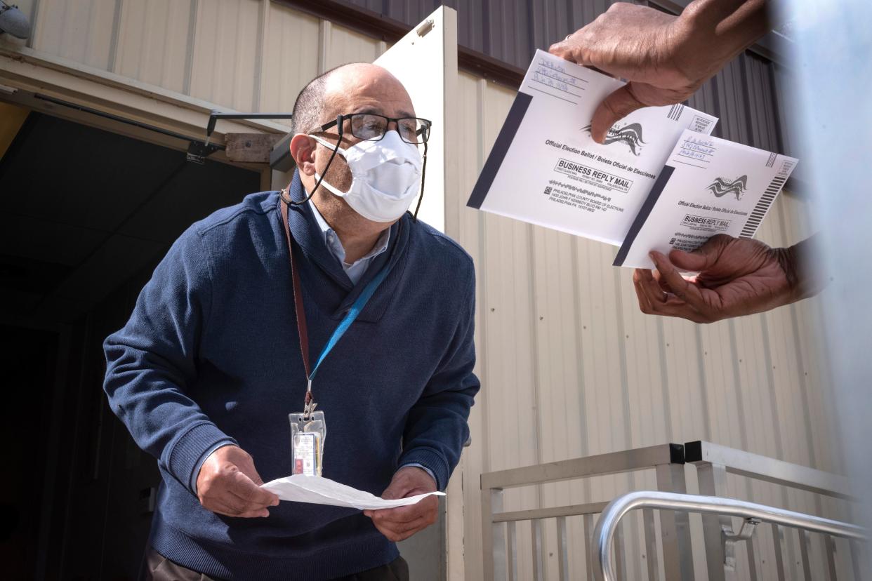 An employee of the Philadelphia Commissioners Office examines ballots at a satellite election office at Overbrook High School in Philadelphia. Local election clerks can’t start verifying mailed-in ballots in Pennsylvania until Election Day and in Michigan until the day before, which the secretary of state says is not enough time.  (AP Photo/Laurence Kesterson )