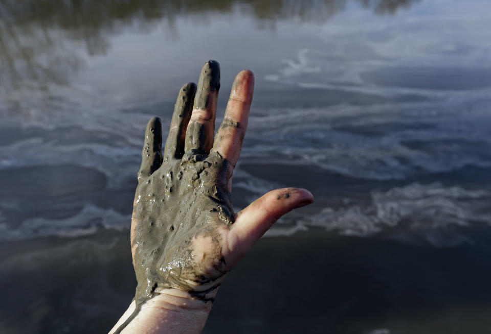 FILE - In this Feb. 5, 2014 file photo, Amy Adams, North Carolina campaign coordinator with Appalachian Voices, shows her hand covered with wet coal ash from the Dan River swirling in the background as state and federal environmental officials continued their investigations of a spill of coal ash into the river in Danville, Va. A federal grand jury is convening Tuesday, March 18, 2014, as part of a widening criminal investigation triggered by the massive Duke Energy coal ash spill that coated 70 miles of the Dan River with toxic sludge. (AP Photo/Gerry Broome, File)