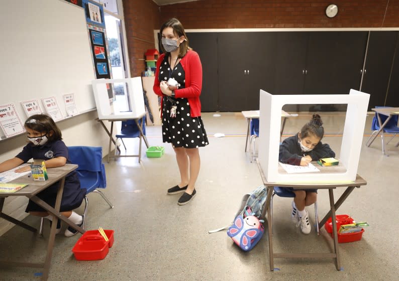 LONG BEACH, CA - OCTOBER 26: Transitional kindergarten and kindergarten teacher Heather Hernandez watches as students Rebecca Dunn, left, and Harper Olloque, right, work in various ways at their desks in the classroom as roughly 40 students returned to St. Maria Goretti Catholic School in Long Beach for in-person instruction Monday with transitional kindergarten and kindergarten returning for full-time in-person instruction and 1st and 2nd grade students adopting a hybrid schedule. St. Maria Goretti is the first Catholic School in Los Angeles County to receive waiver approval to reopen since schools moved to remote learning in March due to the COVID-19 pandemic. St. Maria Goretti Catholic School on Monday, Oct. 26, 2020 in Long Beach, CA. (Al Seib / Los Angeles Times