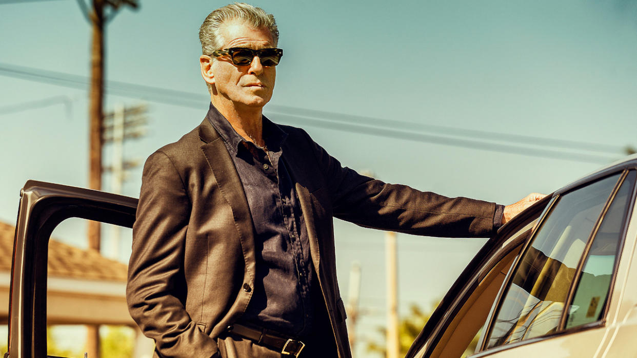  Pierce Brosnan stands next to his car sharply dressed in Fast Charlie. 