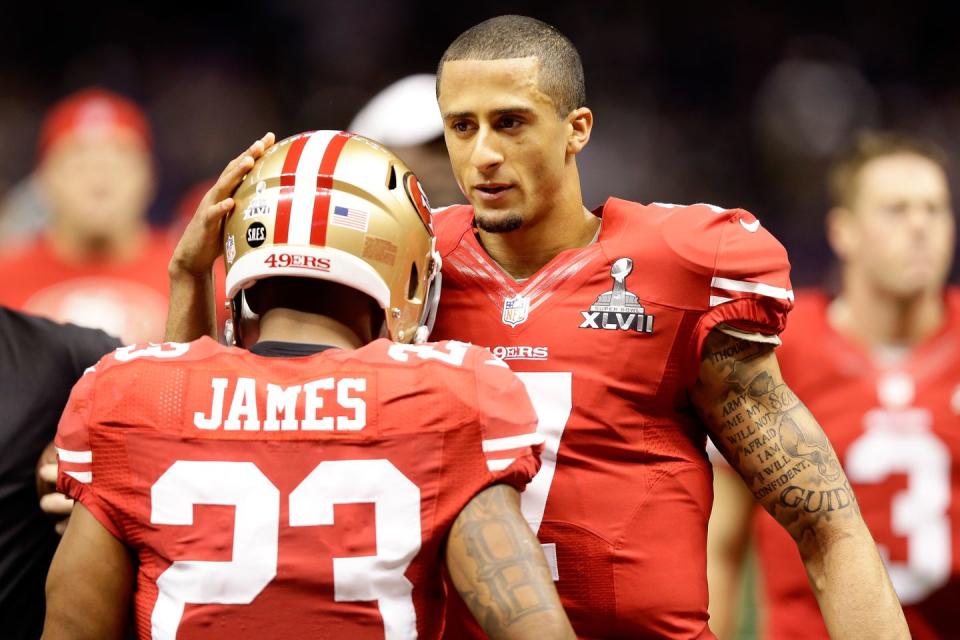 colin kaepernick taps teammate lamichael james on his football helmet, both men wear padding underneath red jerseys