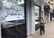 A woman passes a jewelry shop with a sign in the window in Arabic that reads, "We buy gold and pay cash in dollars," in Beirut, Lebanon, Monday, July 6, 2020. Lebanon's financial meltdown has thrown its people into a frantic search for dollars as the local currency's value evaporates. Long, raucous lines mass outside exchange bureaus to buy rationed dollars. With tens of thousands thrown into poverty, the turmoil is fueling bitterness at banks and politicians. (AP Photo/Hussein Malla)