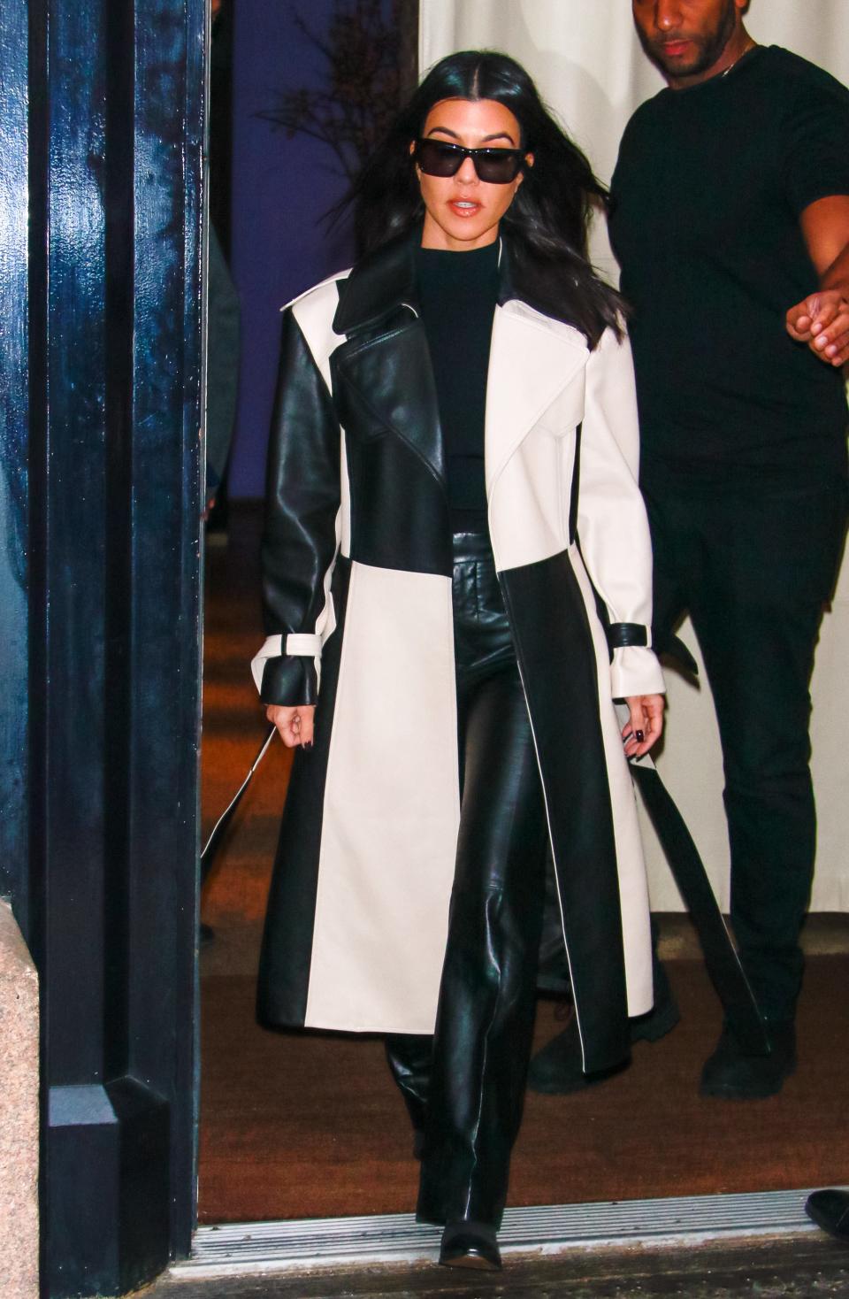 Kortney in a color-block black and white leather trench coat with a black shirt, leather pants, and dark sunglasses.
