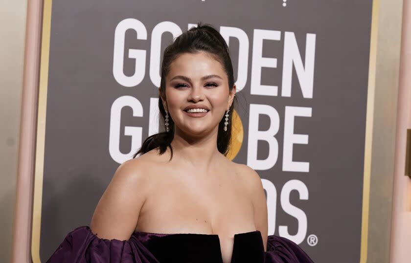 A woman with dark hair smiles for cameras at an awards show wearing a strapless formal gown