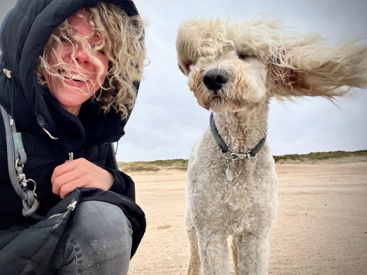 A woman with curly hair poses for a selfie with her dog, who has curly fur.