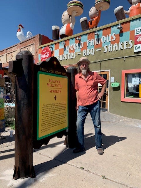 Teako Nunn, owner of Sparkys BBQ and Espresso in Hatch, stands with a replica New Mexico Historic Marker sign that was once a prop at the New Mexico Farm & Ranch Heritage Museum. The sign gives the history of the Sparkys site, and promotes the Farm & Ranch Museum.