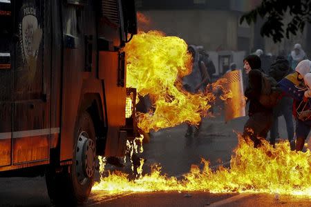 An anti-government protester wearing a Guy Fawkes mask stands with a shield near flames from molotov cocktails thrown at a water cannon by anti-government protesters during riots in Caracas in this April 20, 2014 file photo. REUTERS/Jorge Silva/Files