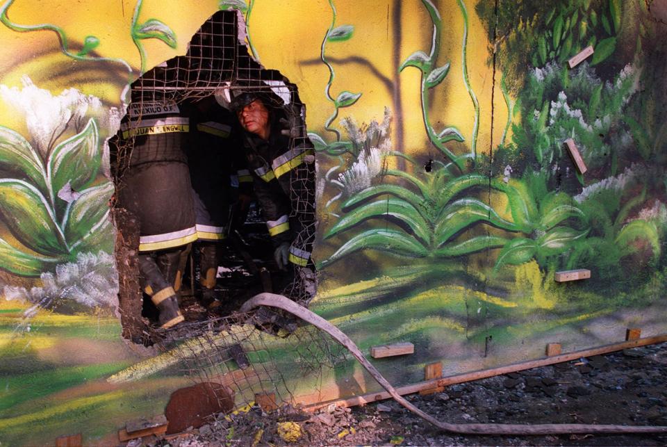 A firefighter looks out from a hole made in the charred facade of the Lobohombo nightclub in Mexico City Friday, Oct. 20, 2000. The city attorney general's office said 19 bodies had been recovered from the club, and at least 24 people were injured. The fire broke out after 5 a.m. and although the cause was not immediately known, firefighters said witnesses reported hearing several explosions. (AP Photo/John Moore)